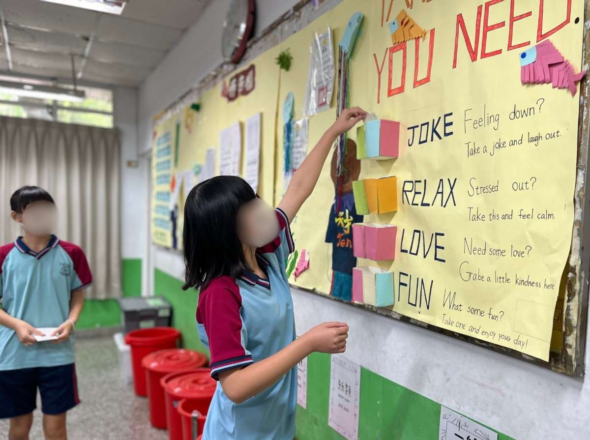 A student sits at a classroom desk with several “Ten Talent” cards placed on the table, preparing to add them to the class activity display.
