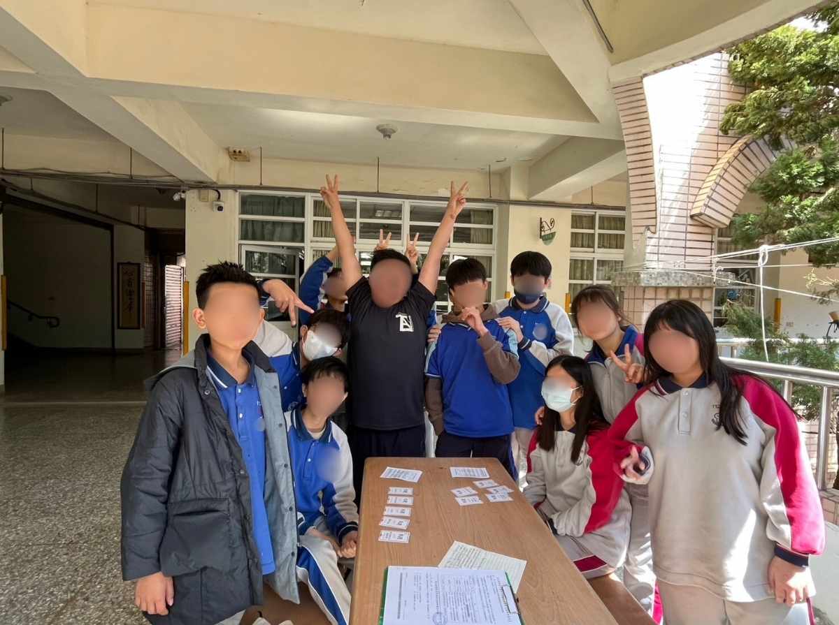 A group of students gathers around a classroom table after completing the personality card game. Cards and worksheets are placed on the table as the students pose together for a group photo.